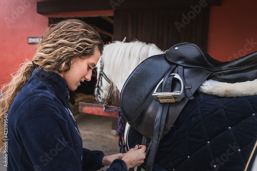 Young caucasian woman preparing a white horse for a ride