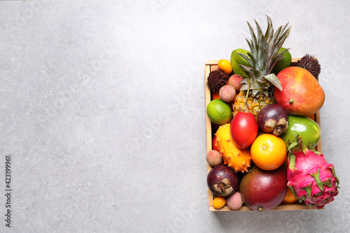 Crate with different exotic fruits on light grey table, top view. Space for text