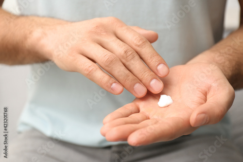 Man applying cream onto hand on blurred background, closeup