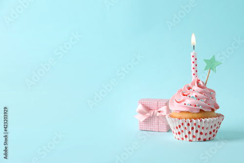 Birthday cupcake with burning candle, gift box and topper on light blue background. Space for text