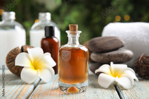 Composition with spa cosmetic and plumeria flowers on light wooden table, closeup