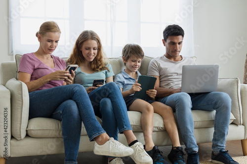 A parent and Children using a laptop, smartphone in the living room.