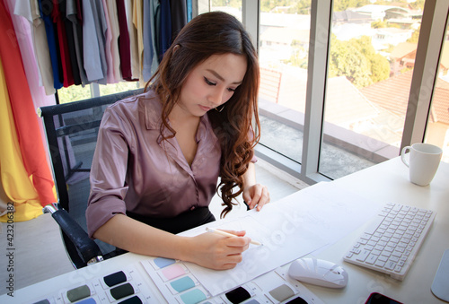 Young asian creative fashion designer  writing an idea on paper in the office after getting an order from customer. Concept of online store, small business, entreprenuer and SME.