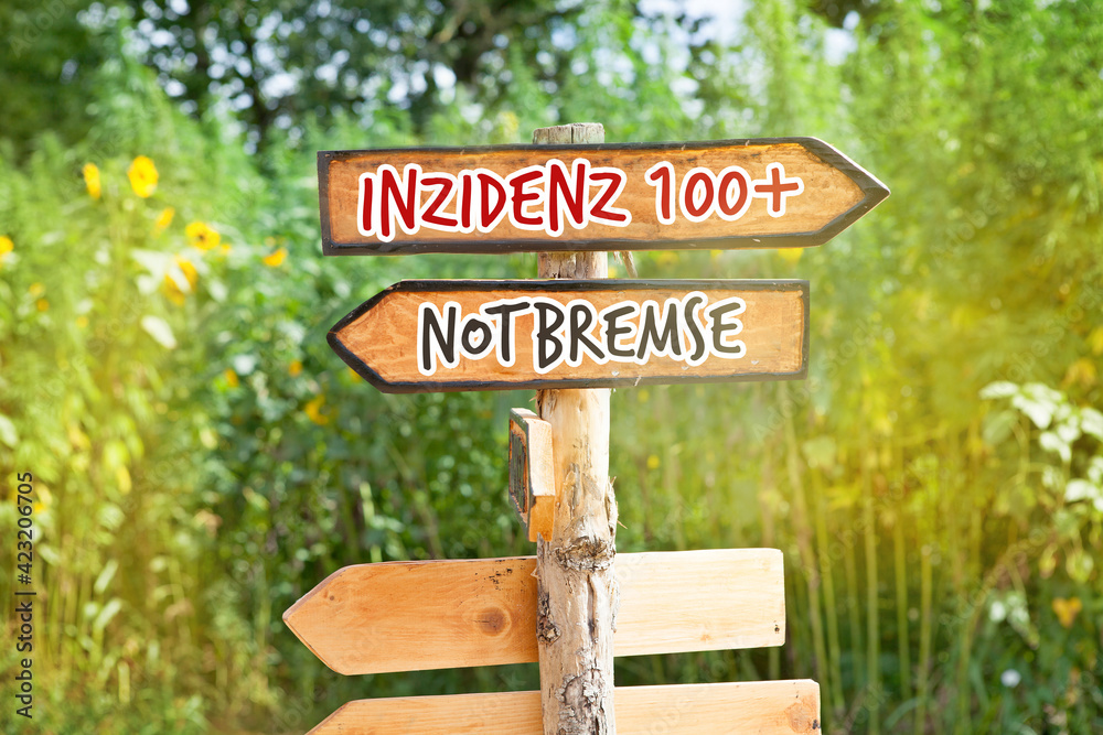 Wooden direction sign with the German words Inzidenz 100+ (incidence 100+) and Notbremse (emergency brake)