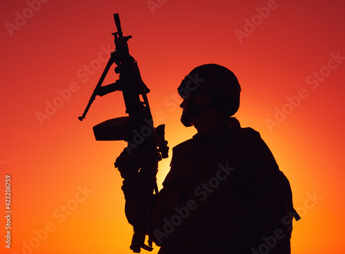 Silhouette of army soldier, special operations shooter armed light machine gun standing on background of ocean or sea horizon at sunset time. Coast guard machine gunner on beach, patrolling coastline