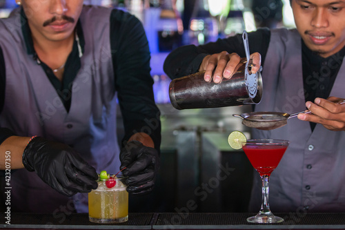 Close up of two expert bartenders are making cocktails at night club or bar