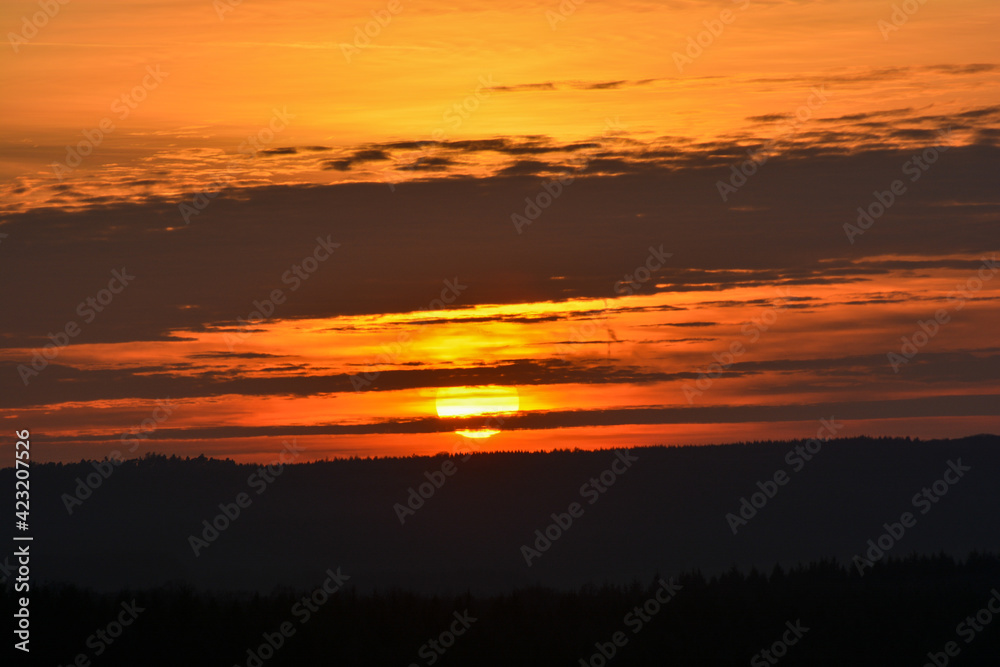 The sun is behind the clouds during an enchanting sunset over a forest near Schweinfurt The sun is behind the clouds during an enchanting sunset over a forest near Schweinfurt