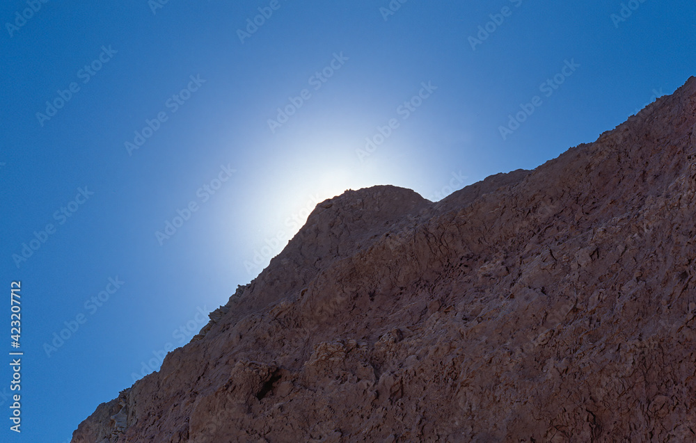 Sun halo and blue summer sky behind mountain