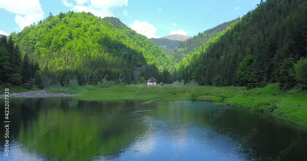 Drone flight above the surface of a mountain lake, in a windy day. The mountain peaks are reflecting into the lake's waters, and the high wind moves the clouds covering in shade the mountain peaks.