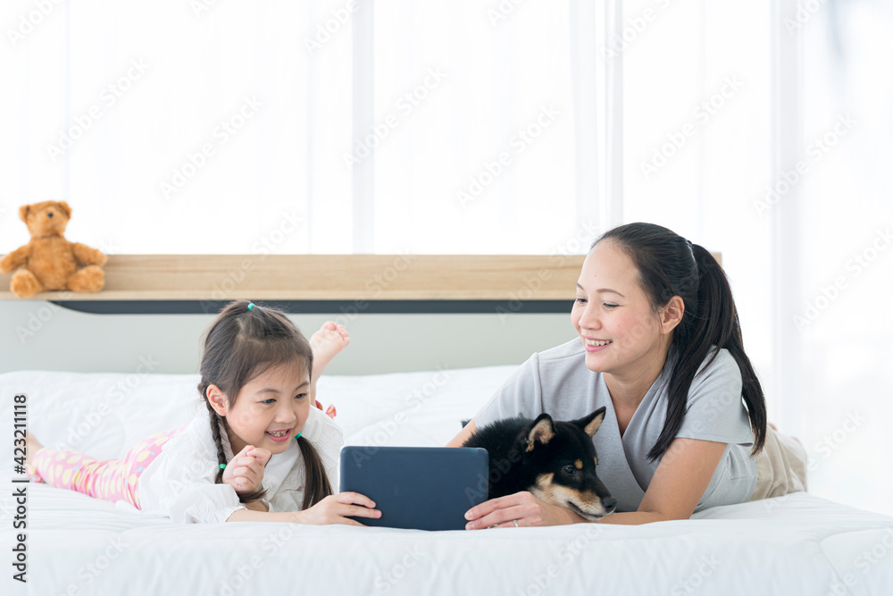 Mom and baby are watching video clips on tablet computers in bed with Shiba Inu. Mom and baby are watching video clips on tablet computers in bed with Shiba Inu.