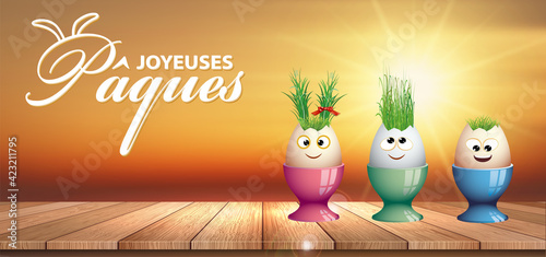 carte ou bandeau sur joyeuses Pâques en blanc représenté par 3 oeufs rigolos mis dans leur coquetier posés sur un plancher de bois  et en fond le coucher du soleil