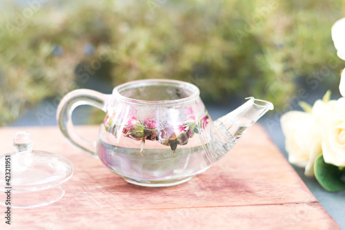 Close-up of a small teapot with rose tea on a wooden stand. Photo in bed colors, a gentle start to the day, a healthy morning drink for women from rosebuds, selective focus.