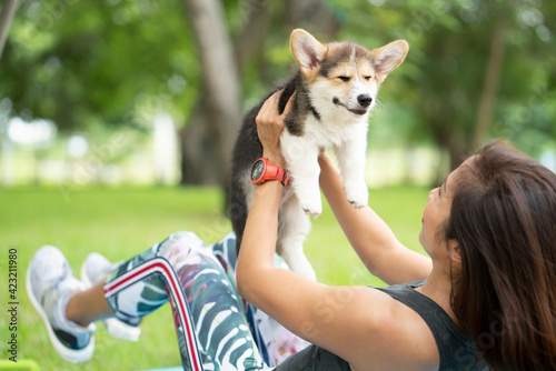 A healthy woman playing with a smiling corgi puppy while excersing on yoga mat, outdoor training with dog