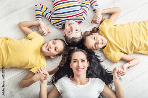 Mom and her three kids hold hands while lying on the floor looking up to the camera
