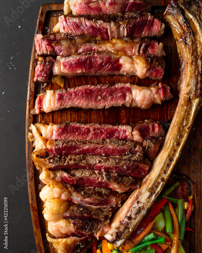 Huge steak with a bone cut into pieces served on wooden board, closeup view