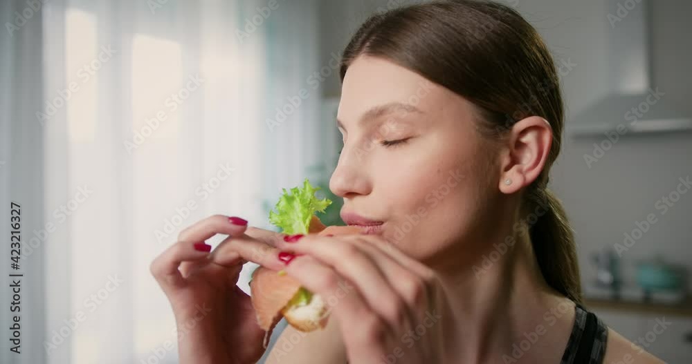 Zoom in shot of attractive young woman snacking on sandwich closing eyes from satisfaction. Healthy eating concept.