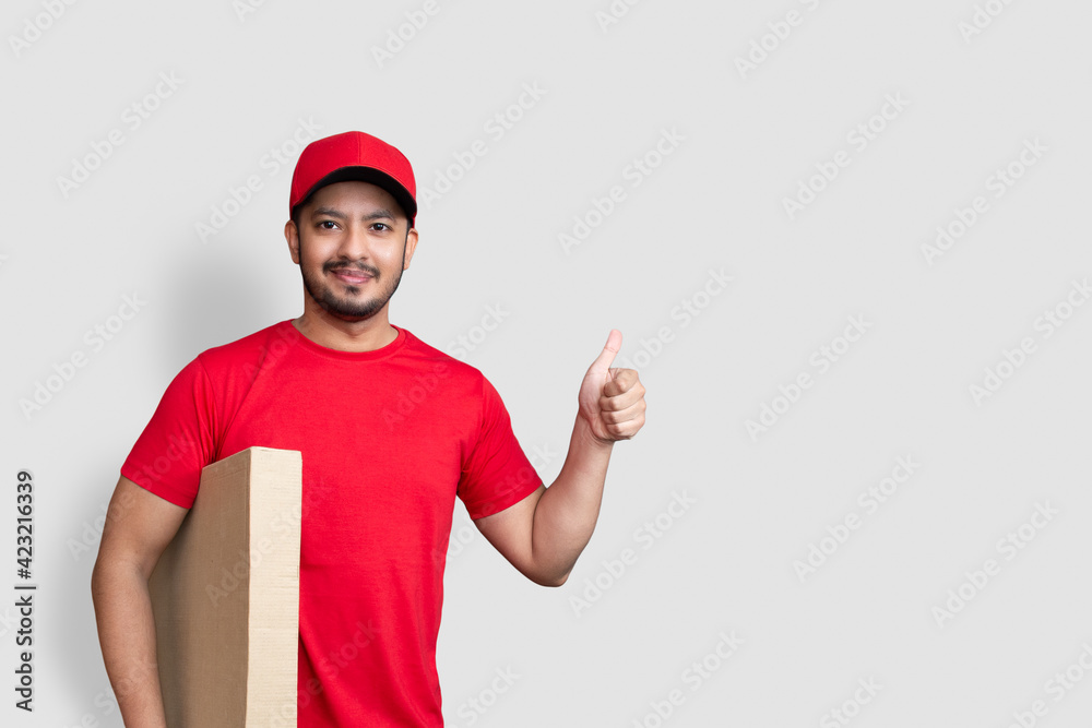 Delivery man employee in red cap blank t-shirt thumbsup uniform hold empty cardboard box isolated on white background Delivery man employee in red cap blank t-shirt thumbsup uniform hold empty cardboard box isolated on white background