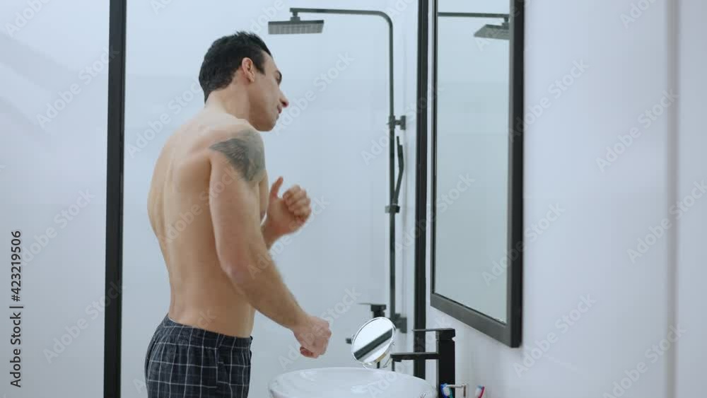 Side view portrait of confident handsome tattooed man adjusting hair looking in mirror in bathroom. Middle shot of fit Middle Eastern guy in the morning at home. Hygiene and lifestyle. Side view portrait of confident handsome tattooed man adjusting hair looking in mirror in bathroom. Middle shot of fit Middle Eastern guy in the morning at home. Hygiene and lifestyle.