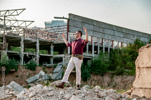 A man in a plaid shirt and sunglasses with sideburns in an abandoned building for demolition walks in military boots