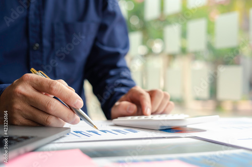 The hand of a male accountant or businessman examining the investment results. And making financial document reports on the desk Business finance accounting concept