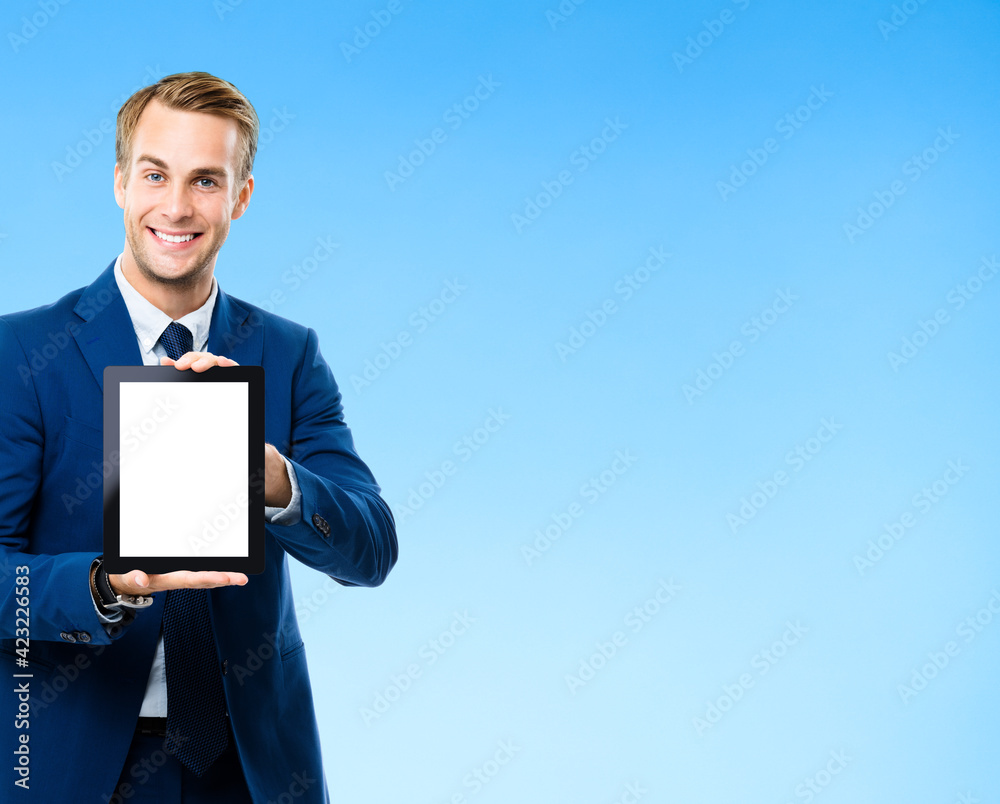 Portrait image of businessman showing blank tablet pc, with copy space area for some text, advertising or slogan, on blue background. Smiling man at business studio concept.