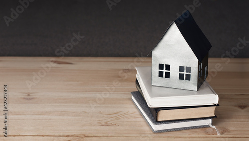 Miniature paper mock-up of a house on a book. Concept of mortgage, rent, purchase, protection, construction of a house. On a wooden background