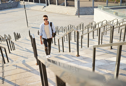man in sunglasses and with a black backpack. Standing on the steps and smiling looks in frame