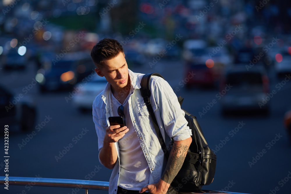 A young guy with a black backpack. Standing on a city street and looking into the phone.