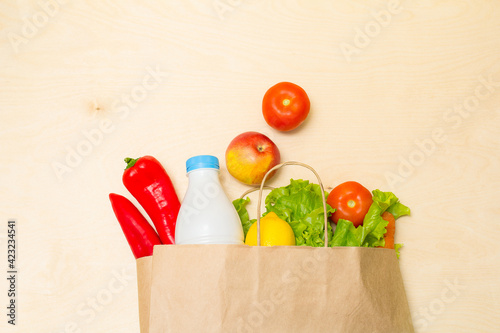 Paper bag with handles full of groceries on wooden background