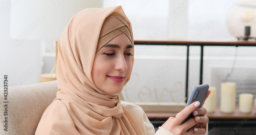 Thoughtful muslim woman in hijab using mobile phone at home Thoughtful muslim woman in hijab using mobile phone at home