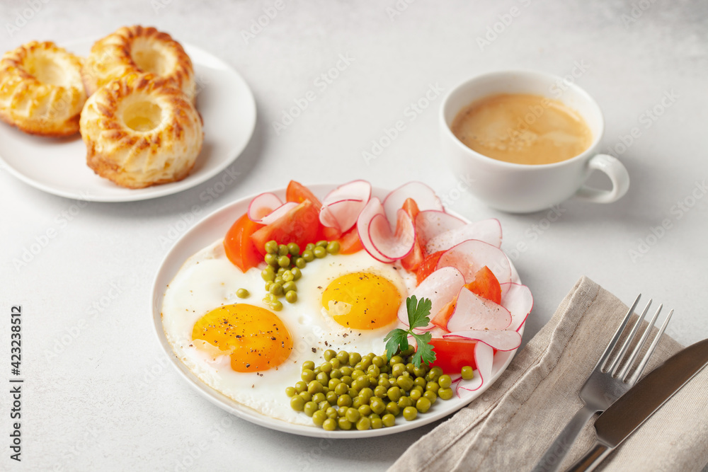 Fried eggs with tomatoes, a radish and green peas in a plate on a table. Healthy breakfast. Cakes and coffee