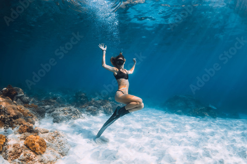 Woman freediver posing over sandy sea with fins