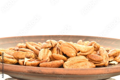 Several light brown organic shelled pecans in a clay plate, close-up, isolated on white.