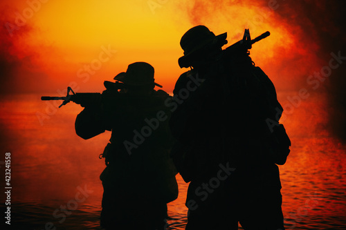 Commando soldiers walking in water, army special operations forces fighters sneaking in darkness, aiming assault rifles and observing shore during amphibious operation on coast at night or dawn photo