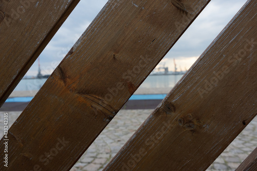 View of the seaport through the planks. Straight lines in perspective, evening landscape on the water and pier © Mariyka LnT