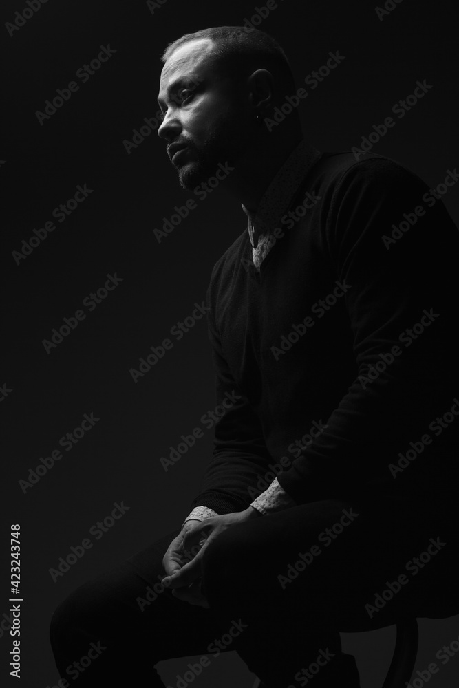 Fabulous at any age. Portrait of charismatic 40-year-old man sitting over black background and waiting. Short haircut. Classic, smart casual style. Black and white studio shot
