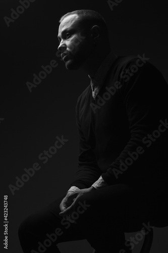 Fabulous at any age. Portrait of charismatic 40-year-old man sitting over black background and waiting. Short haircut. Classic, smart casual style. Black and white studio shot