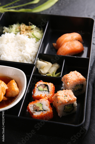 Japanese cuisine. Business lunch in a black box: rice, rolls, salad, sushi on a black table. Background image, copy space