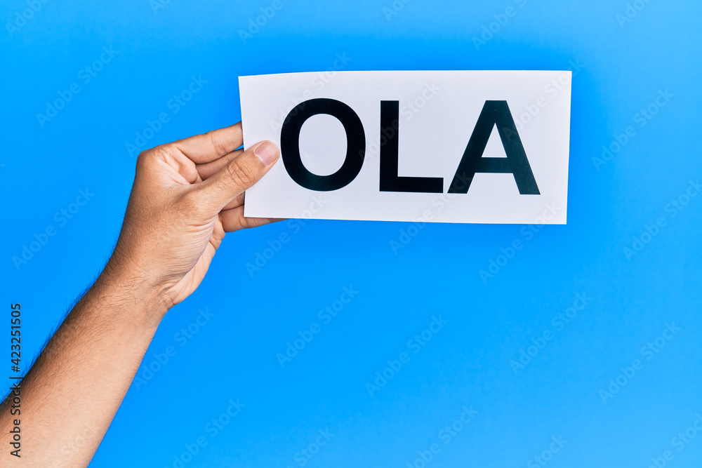 Hand of hispanic man holding ola word paper over isolated blue background. Hand of hispanic man holding ola word paper over isolated blue background.