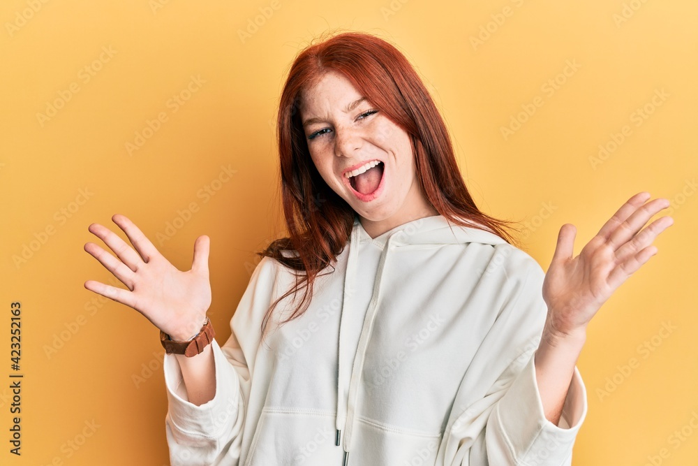 Young red head girl wearing casual sweatshirt celebrating mad and crazy for success with arms raised and closed eyes screaming excited. winner concept Young red head girl wearing casual sweatshirt celebrating mad and crazy for success with arms raised and closed eyes screaming excited. winner concept