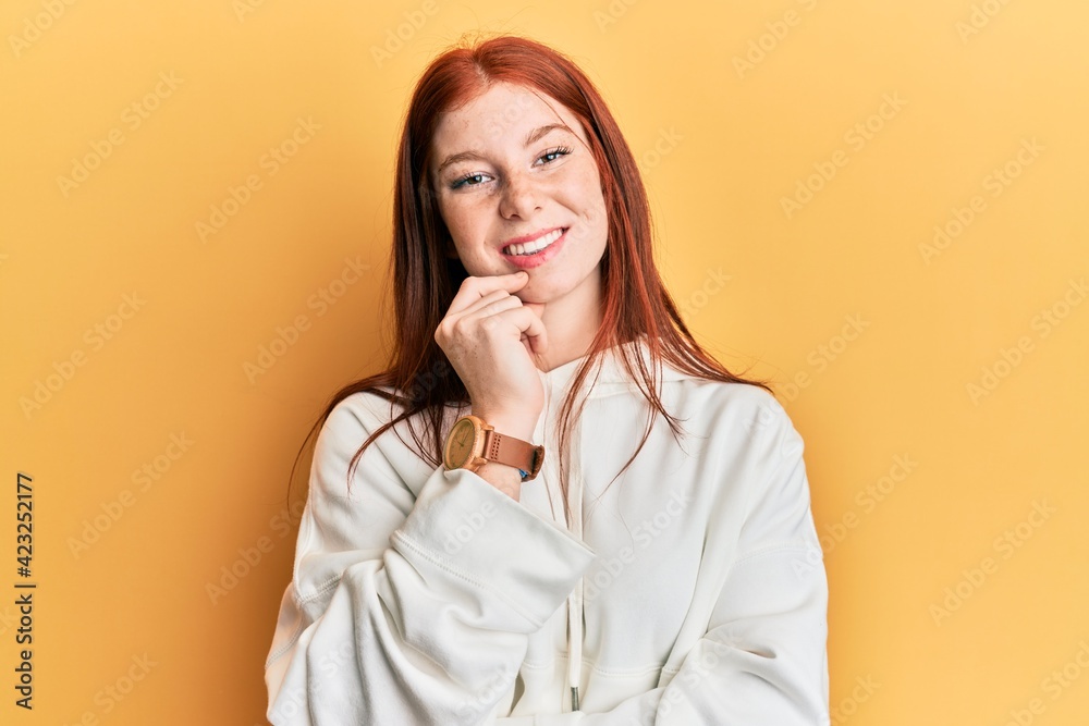 Young red head girl wearing casual sweatshirt looking confident at the camera with smile with crossed arms and hand raised on chin. thinking positive. Young red head girl wearing casual sweatshirt looking confident at the camera with smile with crossed arms and hand raised on chin. thinking positive.