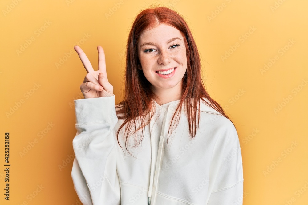 Young red head girl wearing casual sweatshirt showing and pointing up with fingers number two while smiling confident and happy. Young red head girl wearing casual sweatshirt showing and pointing up with fingers number two while smiling confident and happy.