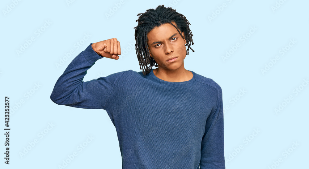 Young african american man wearing casual winter sweater strong person showing arm muscle, confident and proud of power Young african american man wearing casual winter sweater strong person showing arm muscle, confident and proud of power