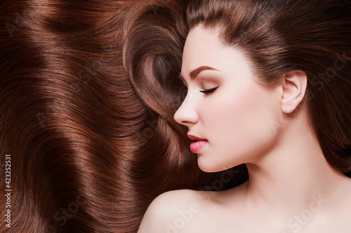 Brown Hair. Beautiful young woman with healthy luxurious long hair on dark background. Hairstyle. Hair cosmetics