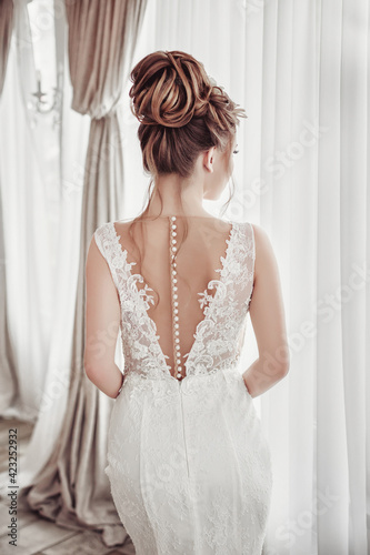 Beautiful bride in wedding dress in luxurious apartment. Fashion makeup and hairstyle. Portrait of young gorgeous bride. Wedding. Studio shot. Back view