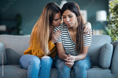 Pretty young woman supporting and comforting her sad friend while sitting on the sofa at home. © nenetus