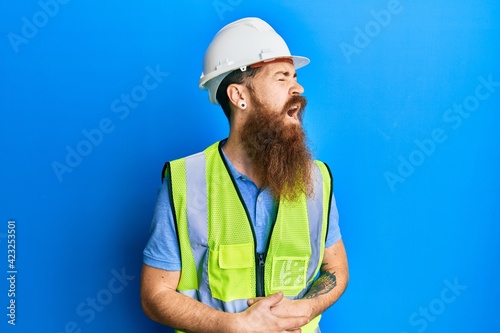Redhead man with long beard wearing safety helmet and reflective jacket with hand on stomach because nausea  painful disease feeling unwell. ache concept.