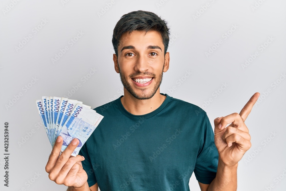 Young handsome man holding 1000 south korean won banknotes smiling happy pointing with hand and finger to the side Young handsome man holding 1000 south korean won banknotes smiling happy pointing with hand and finger to the side