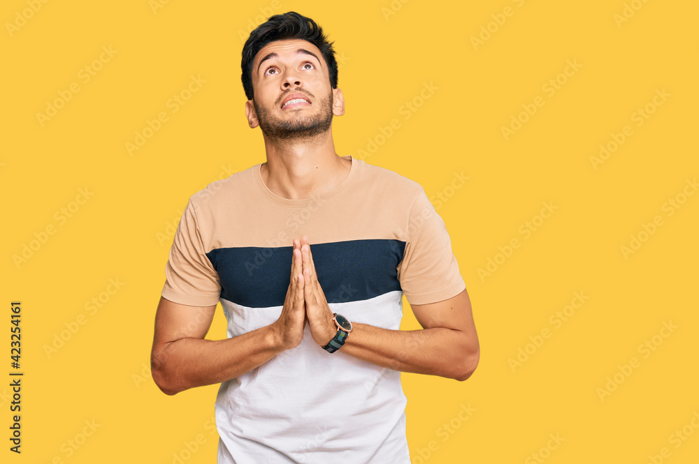 Young handsome man wearing casual clothes begging and praying with hands together with hope expression on face very emotional and worried. begging. Young handsome man wearing casual clothes begging and praying with hands together with hope expression on face very emotional and worried. begging.
