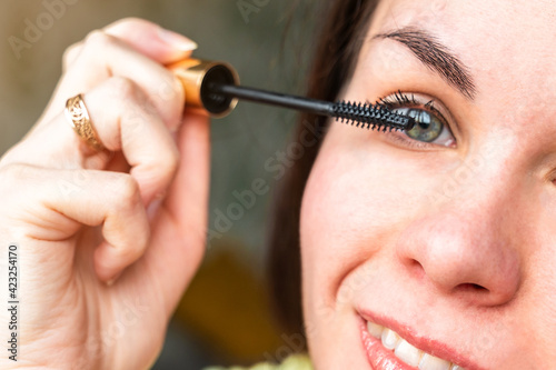 A young woman is doing makeup. Girl paints her eyelashes with mascara